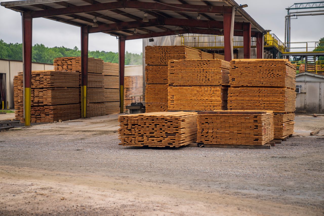 portfolio-06 Stacks of timber planks at an outdoor lumber yard, showcasing construction supplies.