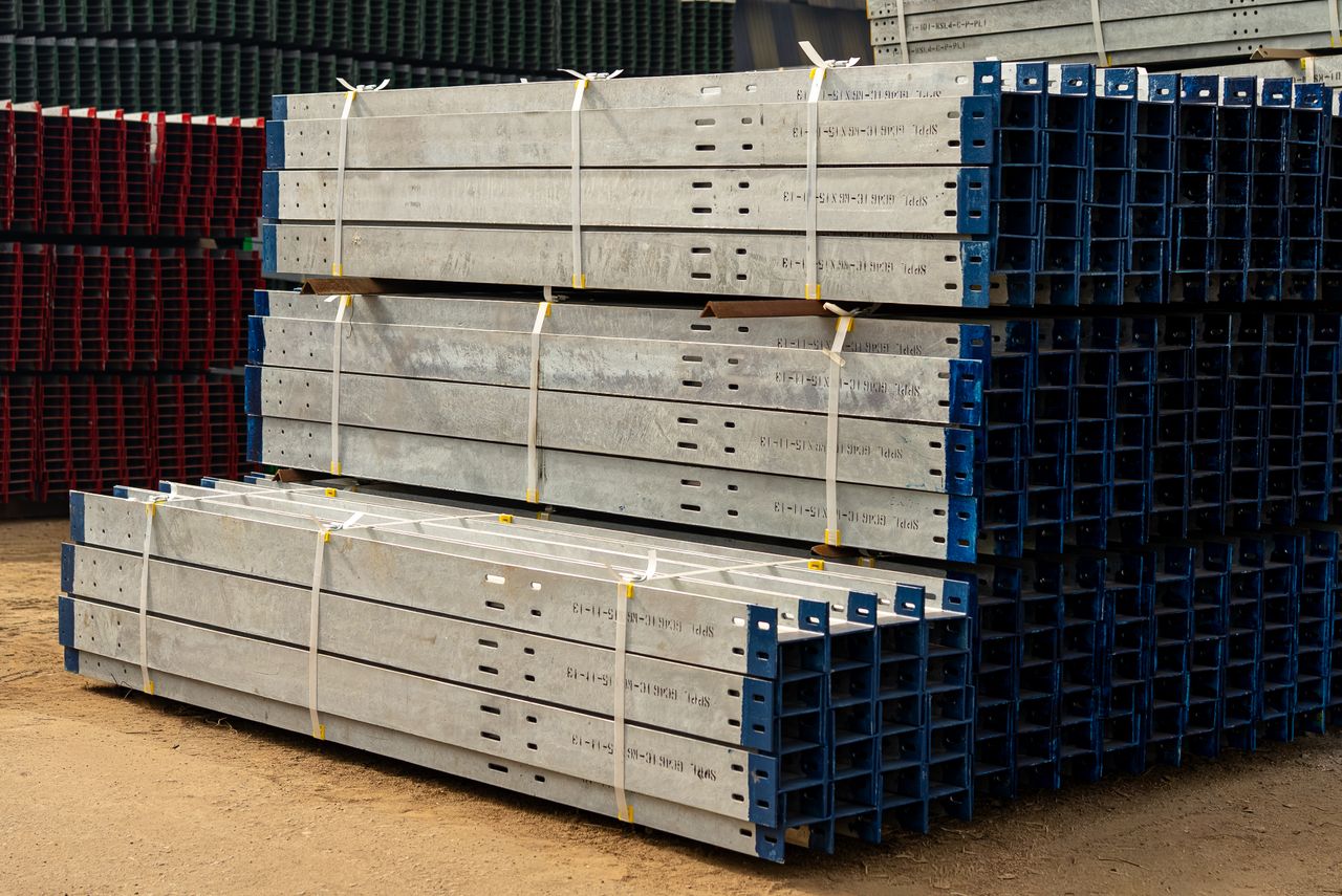 portfolio-04 Neatly stacked metal beams in an outdoor industrial yard under daylight.